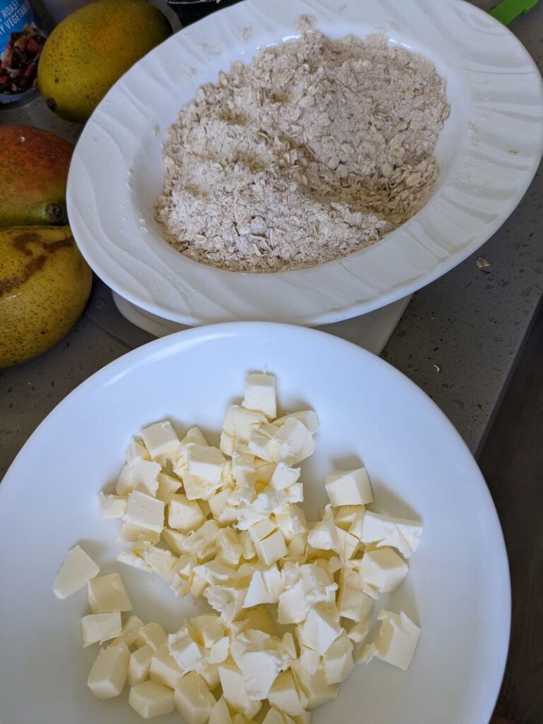 cubes of cold butter in a bowl next to a bowl of oats, flours, and leavening
