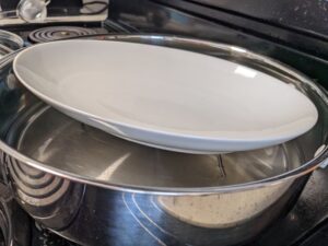 large fry pan with steaming rack, water, and plate set up for steaming fish