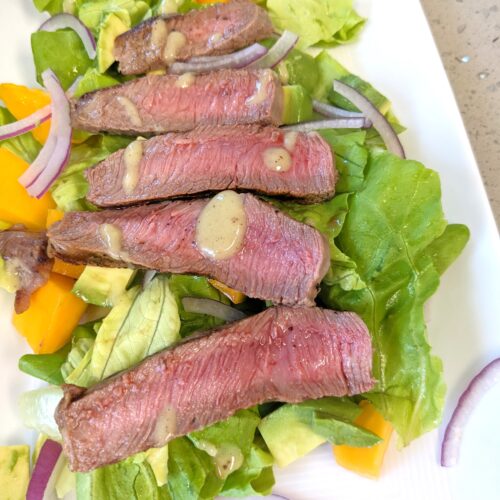 butter lettuce salad topped with grilled steak, red onions, papaya, avocado, and kiwi ginger salad dressing