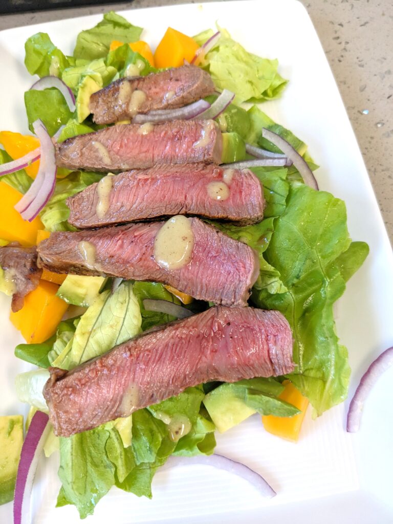 butter lettuce salad topped with grilled steak, red onions, papaya, avocado, and kiwi ginger salad dressing