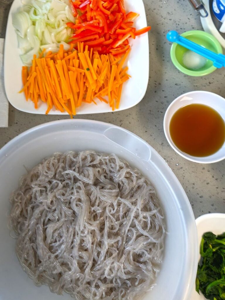 cooked japchae noodles next to raw vegetables for potluck japchae